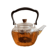 Clear glass teapot with black handle and lid knob with an internal measuring cup for defusing teas and herbs .. the image show the teapot filled with tea