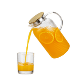 Glass pitcher with gold lid pouring orange juice into a glass